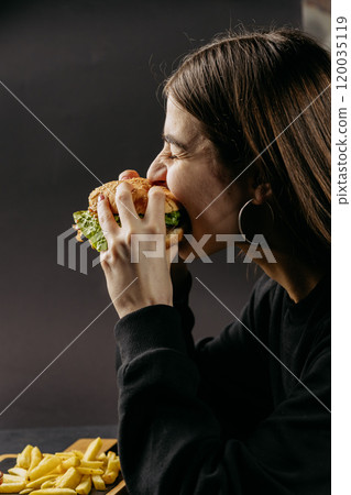 Woman enjoying big juicy burger with a playful expression, indulging in a delicious meal with fries Woman enjoying big juicy burger with a playful expression, indulging in a delicious meal with fries 120035119