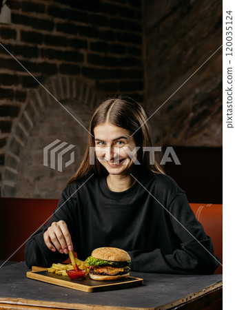 Smiling woman enjoying classic burger and fries with ketchup, creating a perfect comfort food moment 120035124
