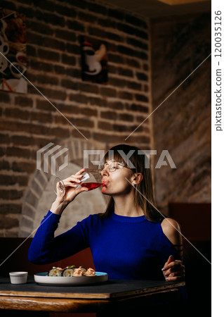 Woman sipping rose wine in a cozy restaurant, enjoying a sophisticated dining moment with sushi 120035126