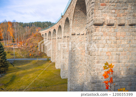 On a sunny autumn day, the impressive railway viaduct in Smrzovka stands tall against a backdrop of colorful foliage in the Jizera Mountains, inviting travelers to explore the stunning landscape. 120035399