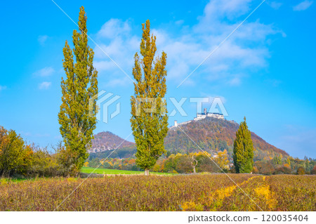 The stunning Bezdez Castle rises majestically on a hill, surrounded by vibrant autumn foliage, under a clear blue sky, showcasing the beauty of the Czech landscape during fall. 120035404