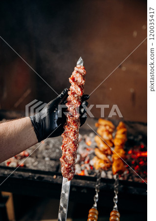 Chef preparing minced meat kebab skewer for grilling over open flame, a classic barbecue delicacy 120035417