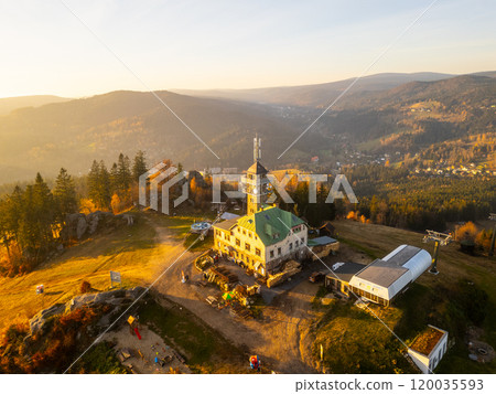 The Tanvaldsky Spicak lookout tower stands prominently in the Jizera Mountains, surrounded by vibrant autumn foliage during a serene evening glow. Visitors are seen enjoying the view. The Tanvaldsky Spicak lookout tower stands prominently in the Jizera Mountains, surrounded by vibrant autumn foliage during a serene evening glow. Visitors are seen enjoying the view. 120035593