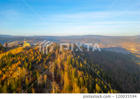 As the sun sets over the Jizera Mountains, the Tanvaldsky Spicak lookout tower stands tall amidst vibrant autumn foliage, offering breathtaking views of the surrounding hills and valleys. 120035594