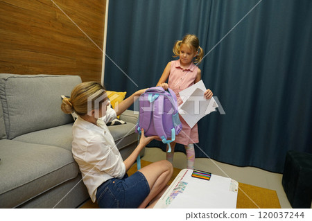 Mother helps her daughter pack her backpack Mother helps her daughter pack her backpack 120037244