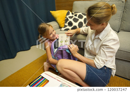 Mother helps her daughter pack her backpack Mother helps her daughter pack her backpack 120037247