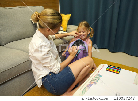 Mother helps her daughter pack her backpack Mother helps her daughter pack her backpack 120037248