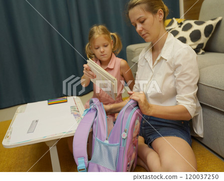 Mother helps her daughter pack her backpack Mother helps her daughter pack her backpack 120037250