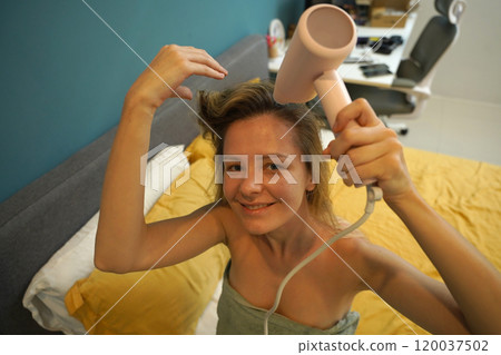 A woman is expertly styling her hair using a blow dryer and brush while in the bathroom 120037502