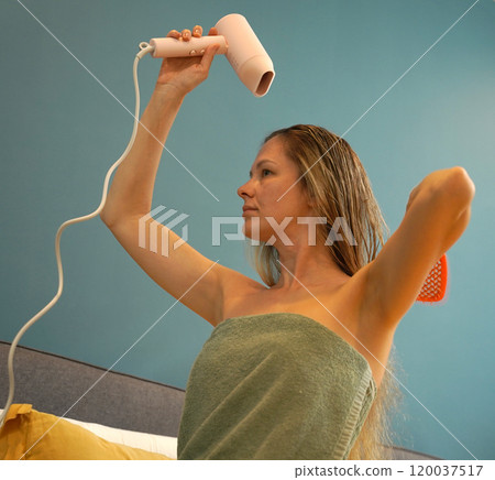 A woman is expertly styling her hair using a blow dryer and brush while in the bathroom A woman is expertly styling her hair using a blow dryer and brush while in the bathroom 120037517