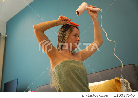 A woman is expertly styling her hair using a blow dryer and brush while in the bathroom 120037540