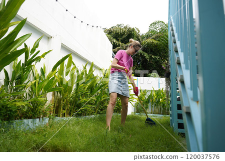 A woman raking the lawn at the backyard of her house A woman raking the lawn at the backyard of her house 120037576
