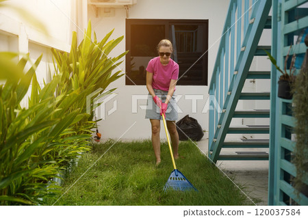 A woman raking the lawn at the backyard of her house A woman raking the lawn at the backyard of her house 120037584