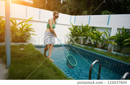 A young woman clean leaves out of a pool A young woman clean leaves out of a pool 120037604