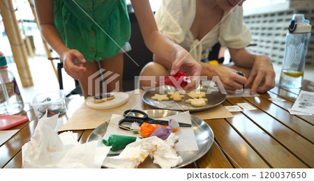 Mother and her daughter paint Halloween cookies  120037650