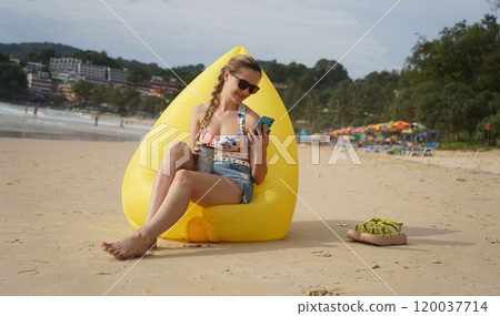 A young woman on the beach lounging on a yellow bean bag  120037714