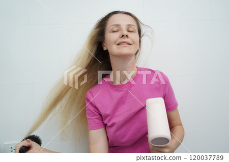 A woman is expertly styling her hair using a blow dryer and brush while in the bathroom 120037789