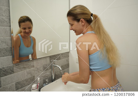 Young woman in a modern bathroom washing her face and brushing her teeth  120037806
