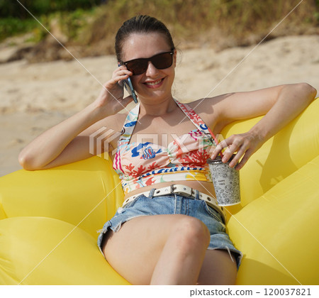 A young woman on the beach lounging on a yellow bean bag  120037821