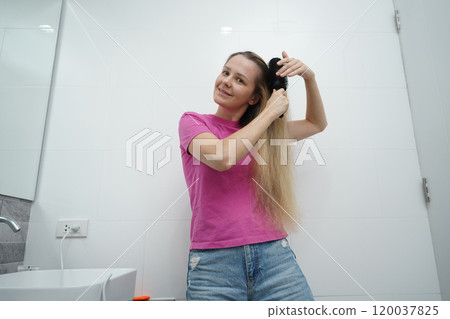 A woman is expertly styling her hair using a blow dryer and brush while in the bathroom A woman is expertly styling her hair using a blow dryer and brush while in the bathroom 120037825