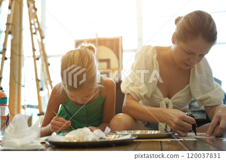 Mother and her daughter paint Halloween cookies  120037831