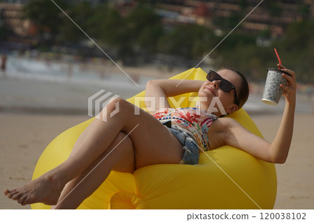 A young woman on the beach lounging on a yellow bean bag A young woman on the beach lounging on a yellow bean bag 120038102