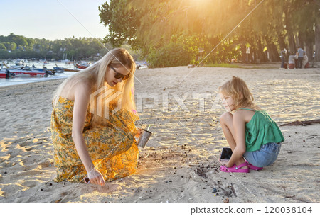A mother and her daughter as they collect shells together  120038104