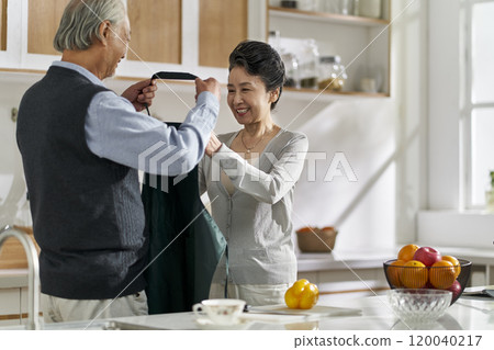 senior asian man helping wife putting on apron senior asian man helping wife putting on apron 120040217
