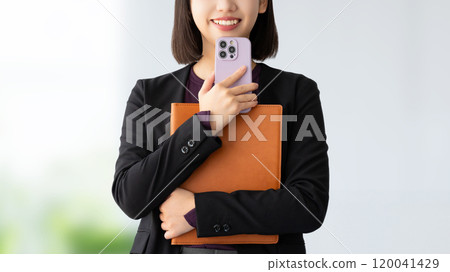 Smiling woman/businesswoman holding a smartphone and a binder 120041429
