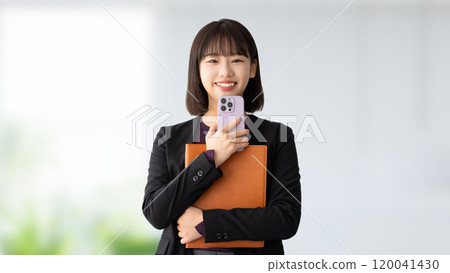 Smiling woman/businesswoman holding a smartphone and a binder Smiling woman/businesswoman holding a smartphone and a binder 120041430