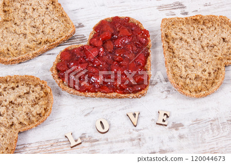 Fresh baked bread in shape of heart with strawberry jam and inscription love. Rustic background 120044673