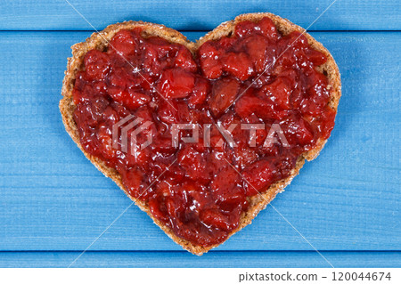 Bread in shape of heart with strawberry jam for breakfast. Blue boards background Bread in shape of heart with strawberry jam for breakfast. Blue boards background 120044674
