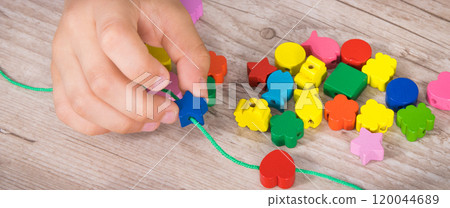 Preschooler making bracelet from thread and wooden colored beads Preschooler making bracelet from thread and wooden colored beads 120044689