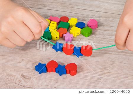 Preschooler making bracelet from thread and wooden colored beads 120044690