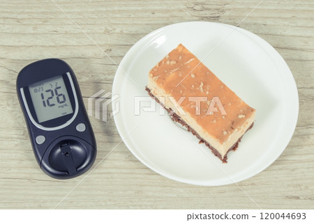Glucometer with high result sugar level and portion of sweet cheesecake. Nutrition during diabetes 120044693