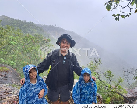 Children and father hiking in the mountains or forest with backpacks in the rainy season and walking sticks. Children and father hiking in the mountains or forest with backpacks in the rainy season and walking sticks. 120045708