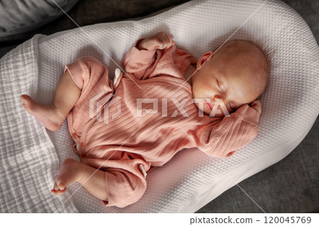 Adorable Newborn Baby Girl in Pink Clothing Sleeping Peacefully While Nestled in Cozy White Cocoon, Serene Moment of Innocence and Comfort in Cozy Indoors 120045769