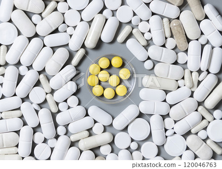 White medical capsules and pills with yellow pills in the middle on grey top view White medical capsules and pills with yellow pills in the middle on grey top view 120046763