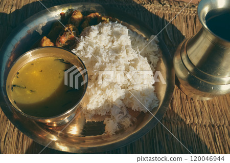 Dal bhat which is rice with lentil soup and chicken curry served on a brass plate known as chares or kaas ko thaal on a rustic straw mat showing the authentic traditional local nepali daily staple foo Dal bhat which is rice with lentil soup and chicken curry served on a brass plate known as chares or kaas ko thaal on a rustic straw mat showing the authentic traditional local nepali daily staple foo 120046944