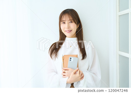 Young woman holding a notebook and smartphone Young woman holding a notebook and smartphone 120047246