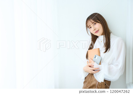 Young woman holding a notebook and smartphone Young woman holding a notebook and smartphone 120047262