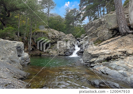 Waterfall at the Cascades des Anglais in Corsica surrounded by rocky terrain and lush forest scenery 120047910