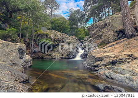 Waterfall at the Cascades des Anglais in Corsica surrounded by rocky terrain and lush forest scenery 120047912
