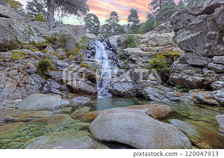 Waterfall at the Cascades des Anglais in Corsica surrounded by rocky terrain and lush forest scenery 120047913