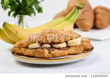 Croissant with chocolate spread and banana pieces in a white round plate on the table, breakfast Croissant with chocolate spread and banana pieces in a white round plate on the table, breakfast 120048930