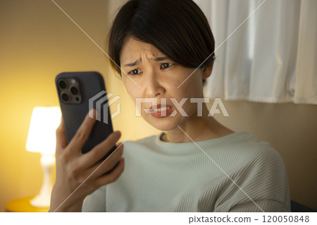 A young woman is surprised at her smartphone at night 120050848