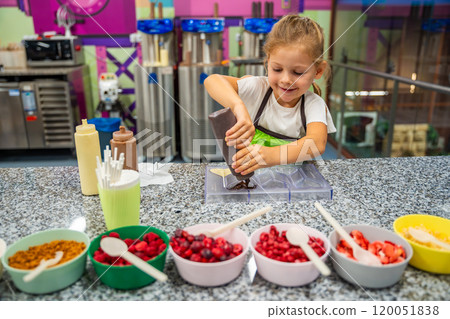 Little girl learning how to cook in a cooking class. Handmade dessert. Making chocolate candy, Child filling heart shaped mold with chocolate 120051838