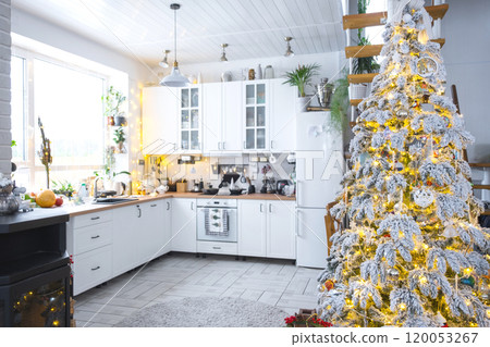 Festive Christmas decor in white kitchen, modern village interior with a snowy Christmas tree and fairy lights. New Year, Christmas mood, cozy home, Metal modular staircase. The general plan Festive Christmas decor in white kitchen, modern village interior with a snowy Christmas tree and fairy lights. New Year, Christmas mood, cozy home, Metal modular staircase. The general plan 120053267