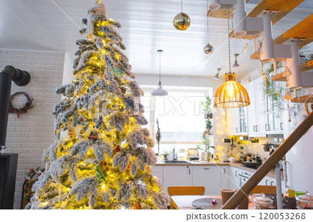 Festive Christmas decor in white kitchen, modern village interior with a snowy Christmas tree and fairy lights. New Year, Christmas mood, cozy home, Metal modular staircase. The general plan 120053268