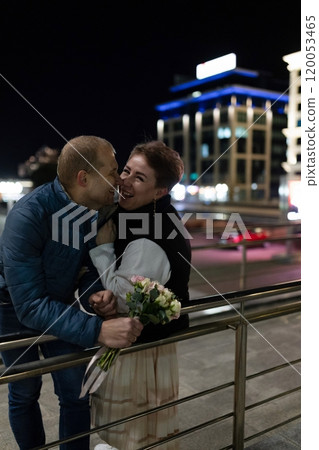 A couple strolls through a city at night, laughing and holding a bouquet of flowers 120053465